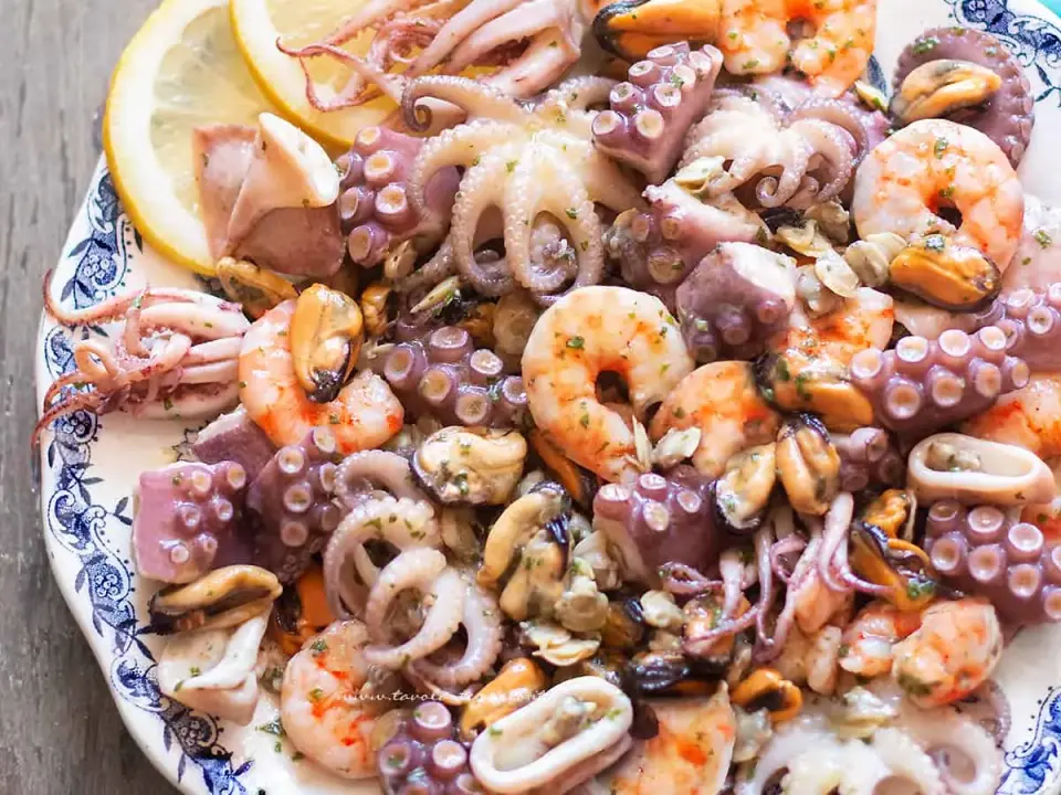 Un invitante piatto di insalata di mare, con polipetti, gamberi e cozze, guarnito con spicchi di limone.